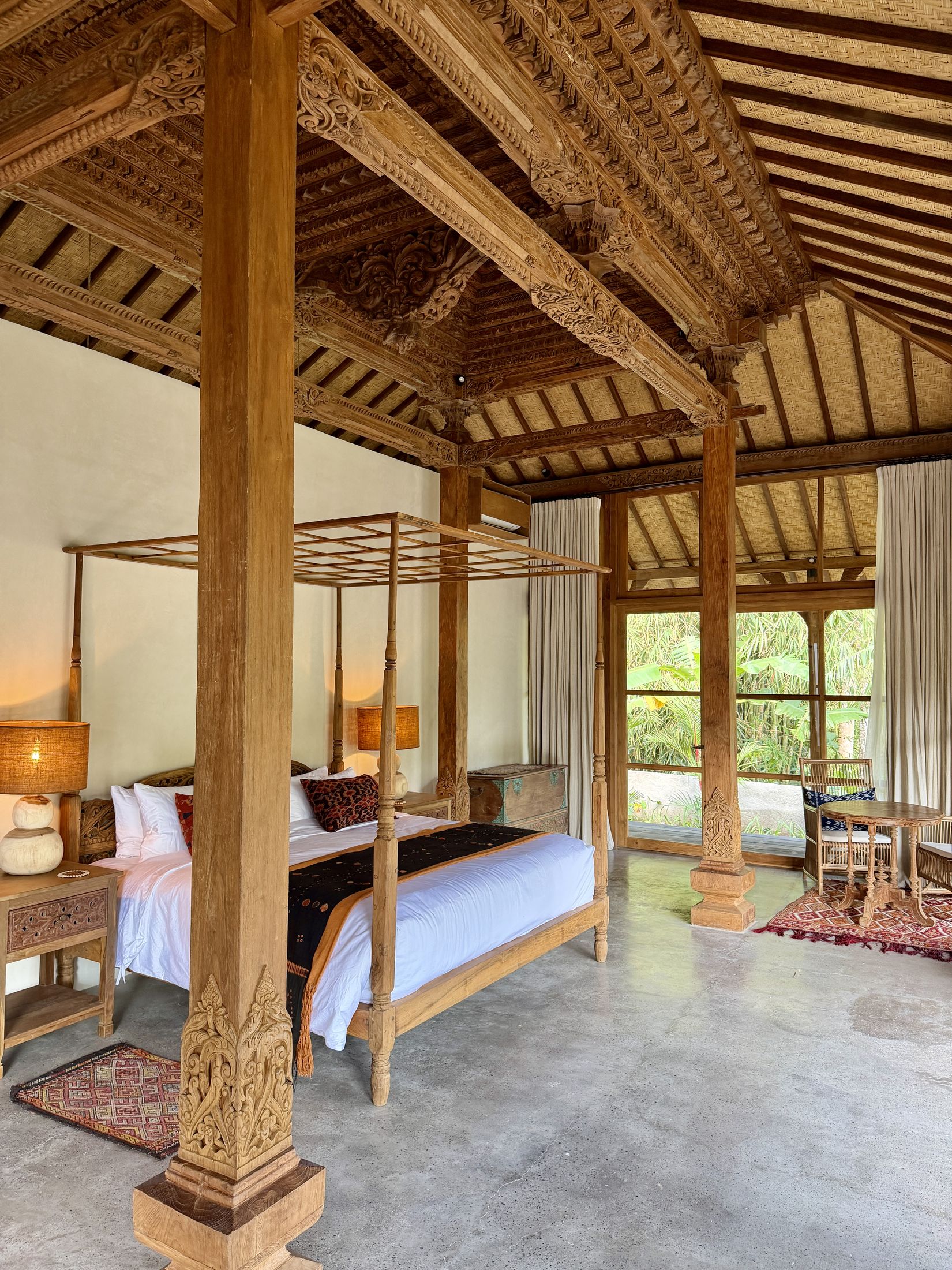 Carved four-poster canopy bed beneath the joglo's hand-carved ceiling