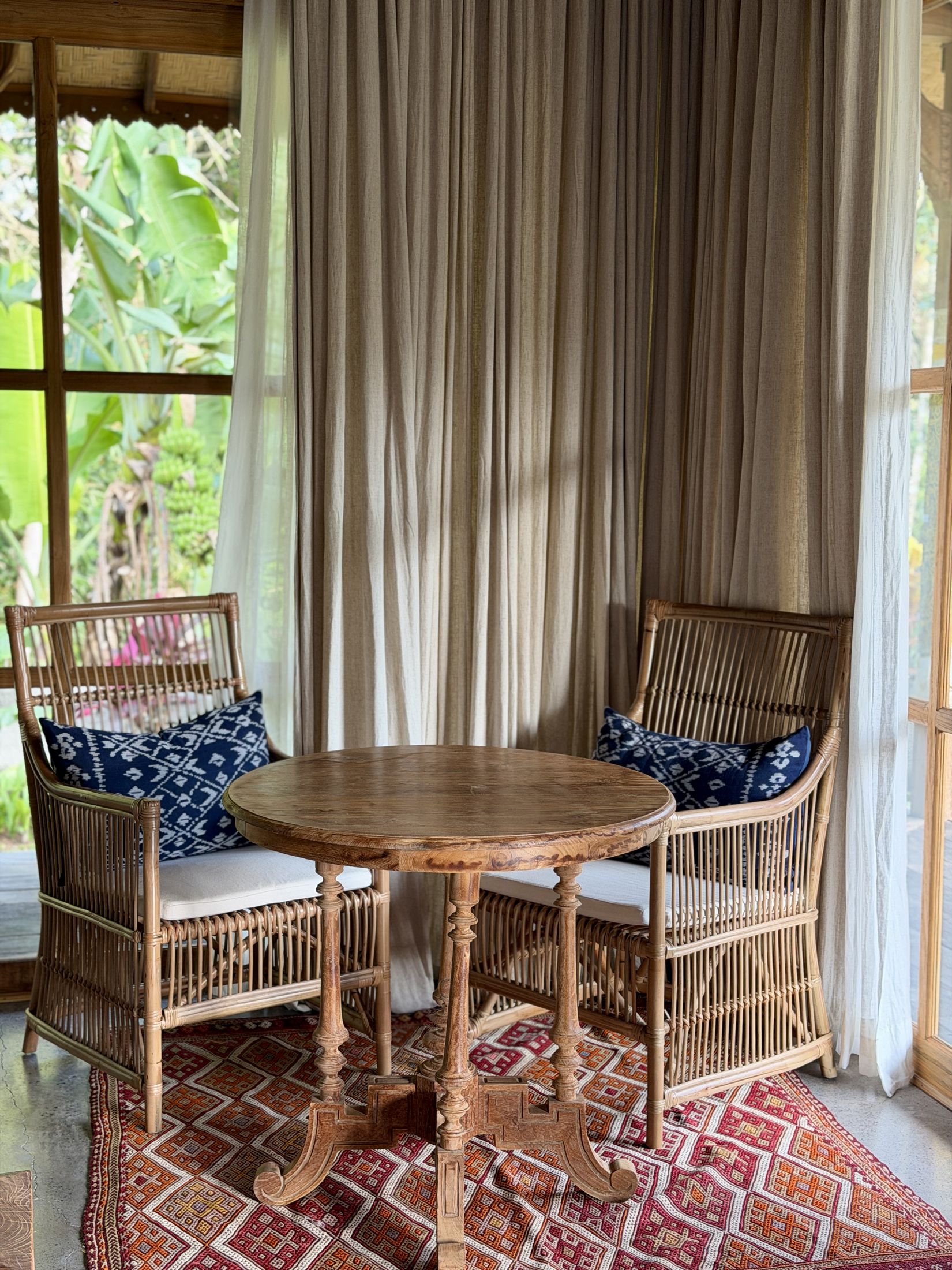 A pair of rattan armchairs around a round table, dressed with indigo ikat pillows