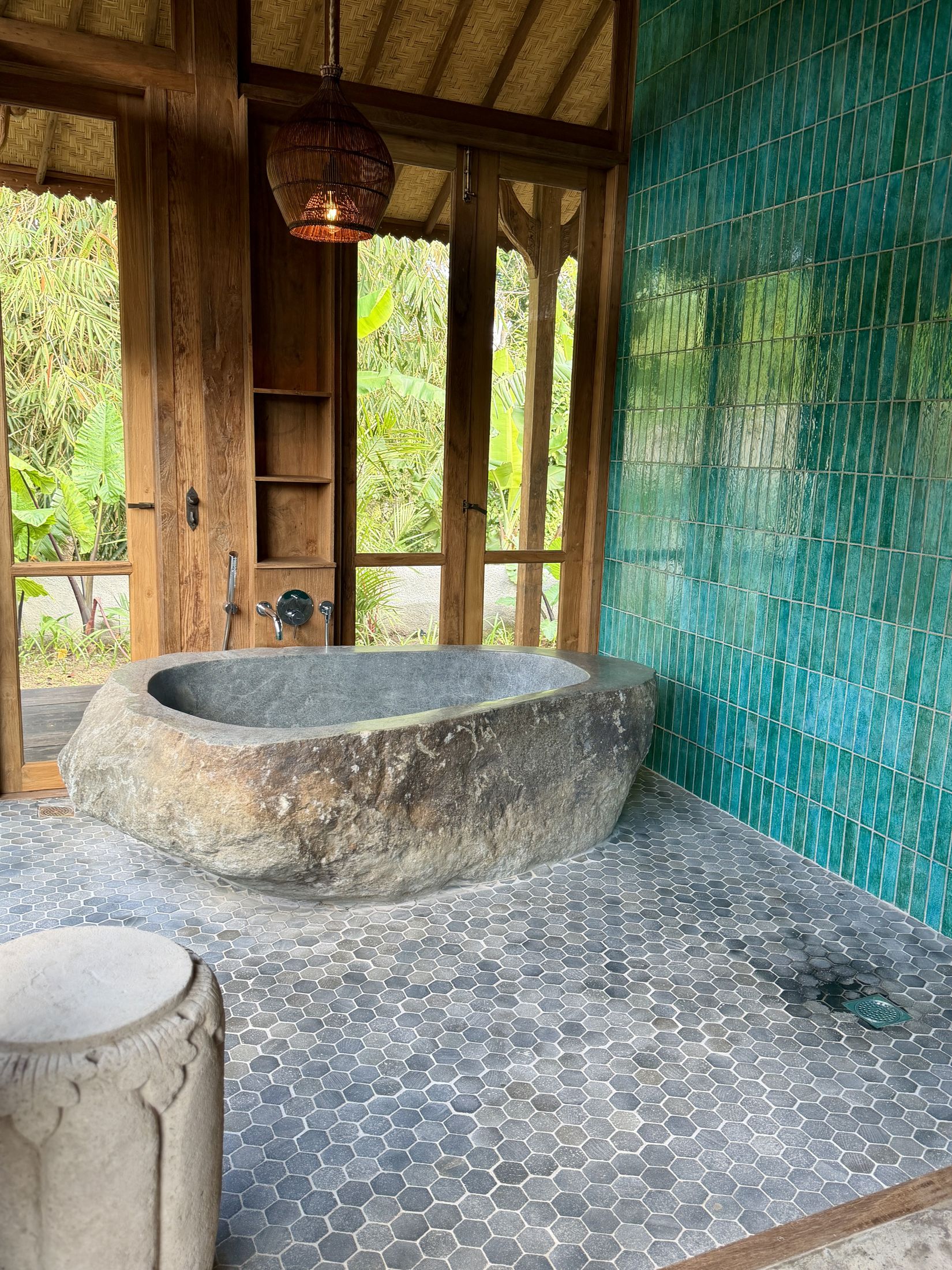 River stone soaking tub and teal-tiled wall in the Primary Joglo bathroom